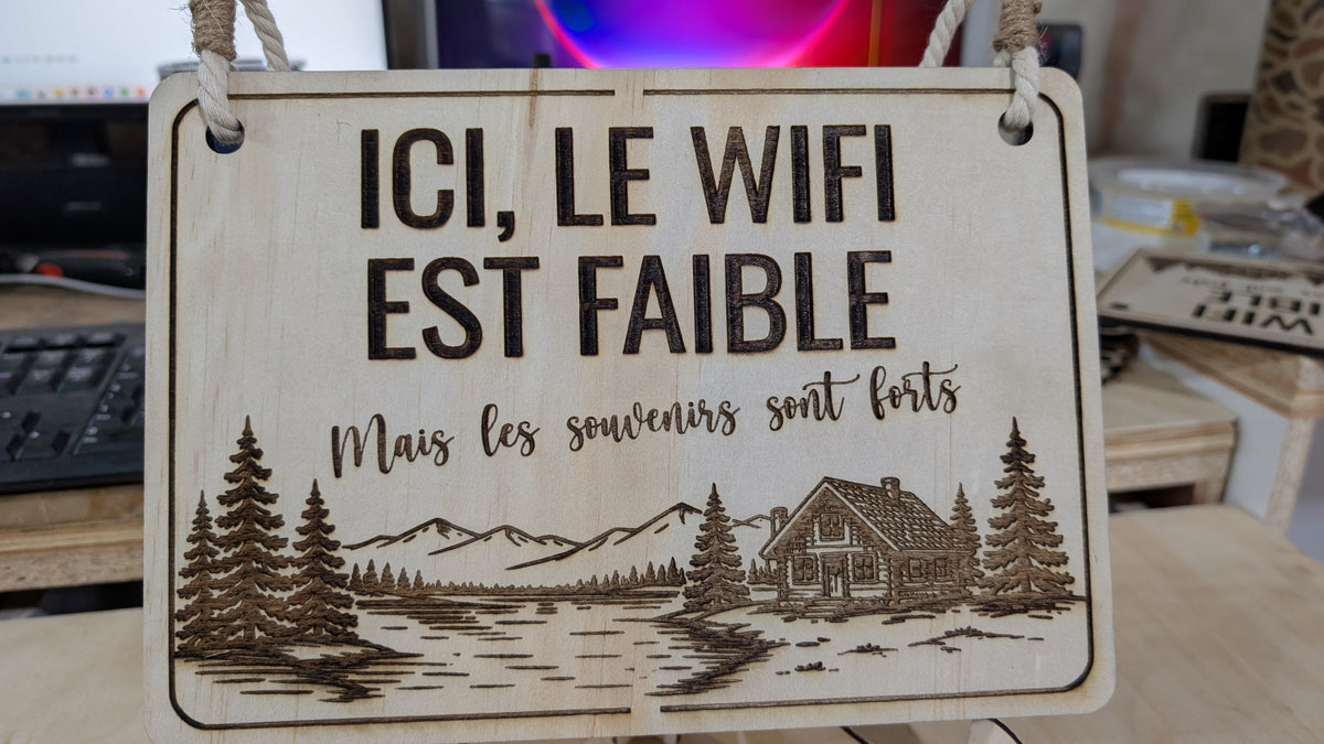 Panneau en bois gravé « Ici, le WiFi est faible, mais les souvenirs sont forts », avec chalet, lac, montagnes et sapins.