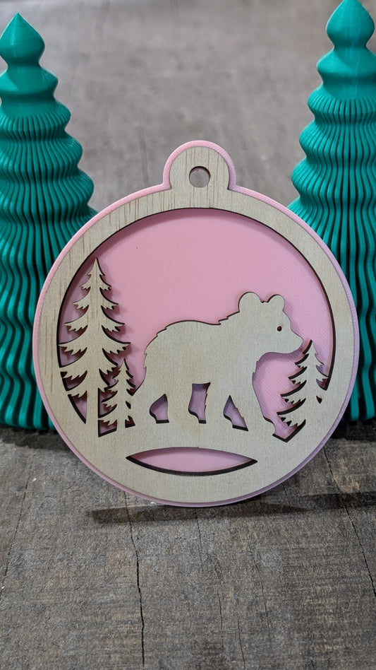 Boule de Noël avec ours et sapins en bois sur fond rose, fabriquée au Québec.