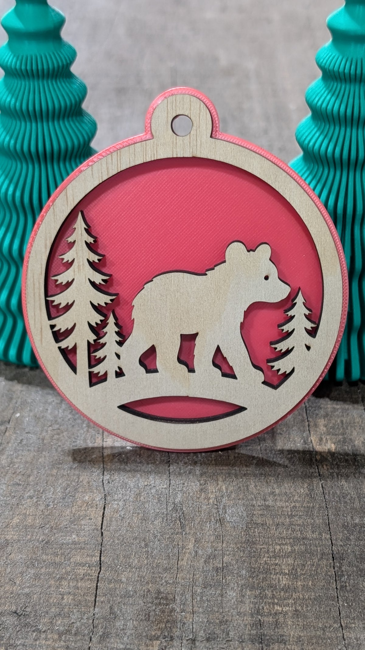Boule de Noël avec ours et sapins en bois sur fond rouge, fabriquée au Québec.