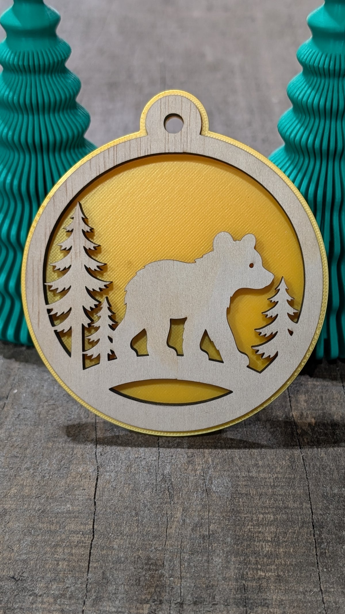 Boule de Noël avec ours et sapins en bois sur fond jaune, fabriquée au Québec.