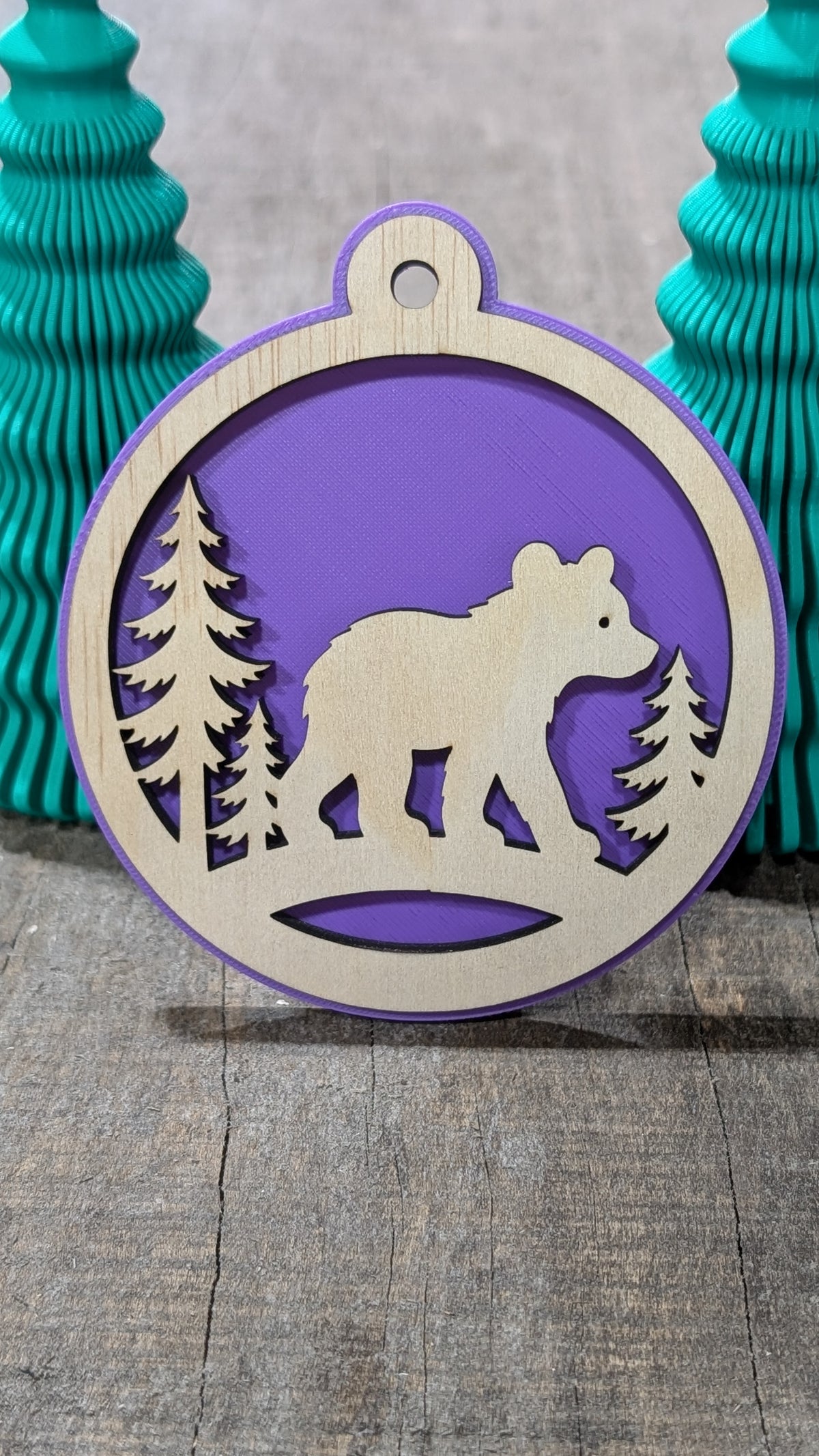 Boule de Noël avec ours et sapins en bois sur fond mauve, fabriquée au Québec.