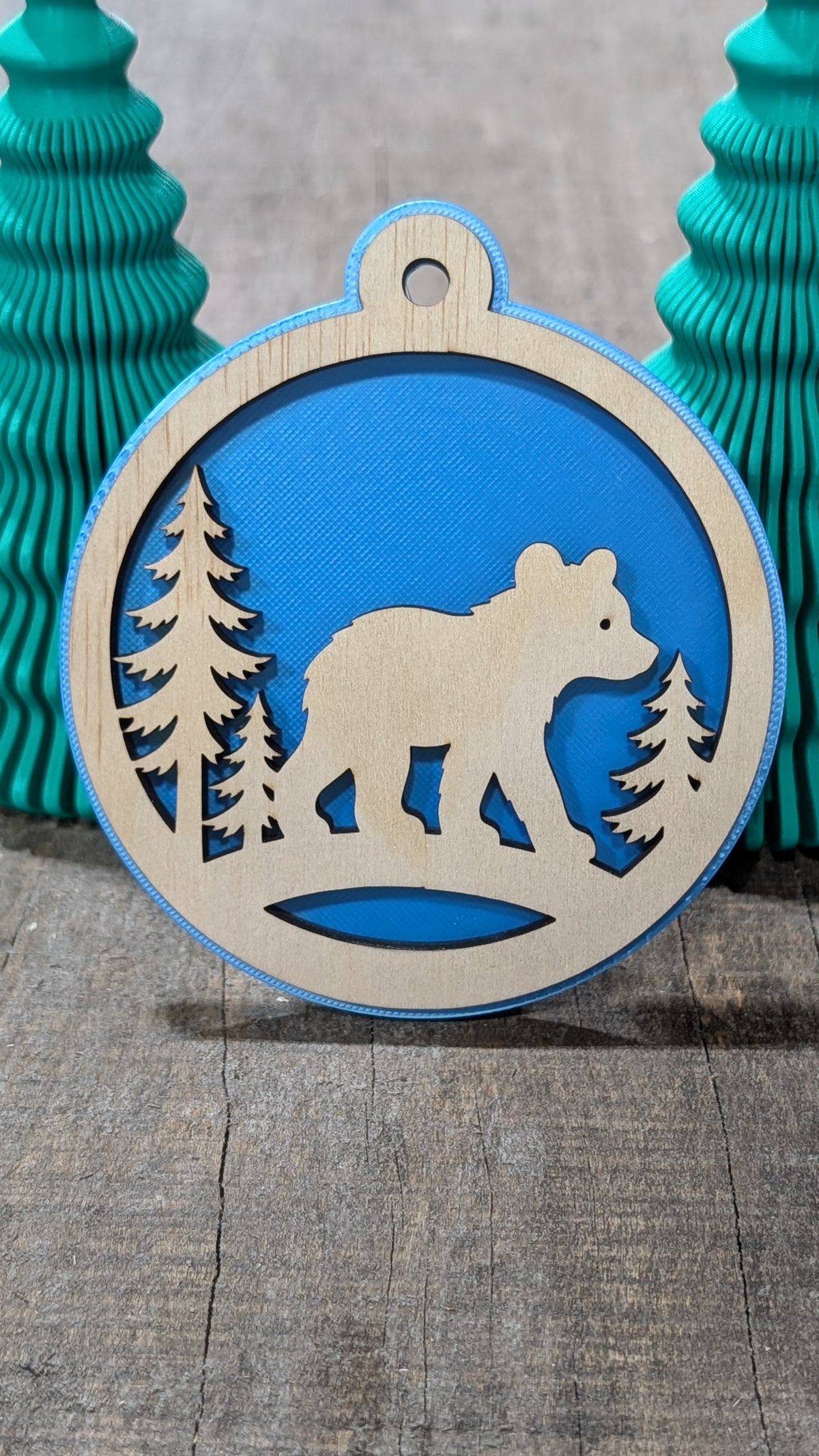 Boule de Noël avec ours et sapins en bois sur fond bleu, fabriquée au Québec.