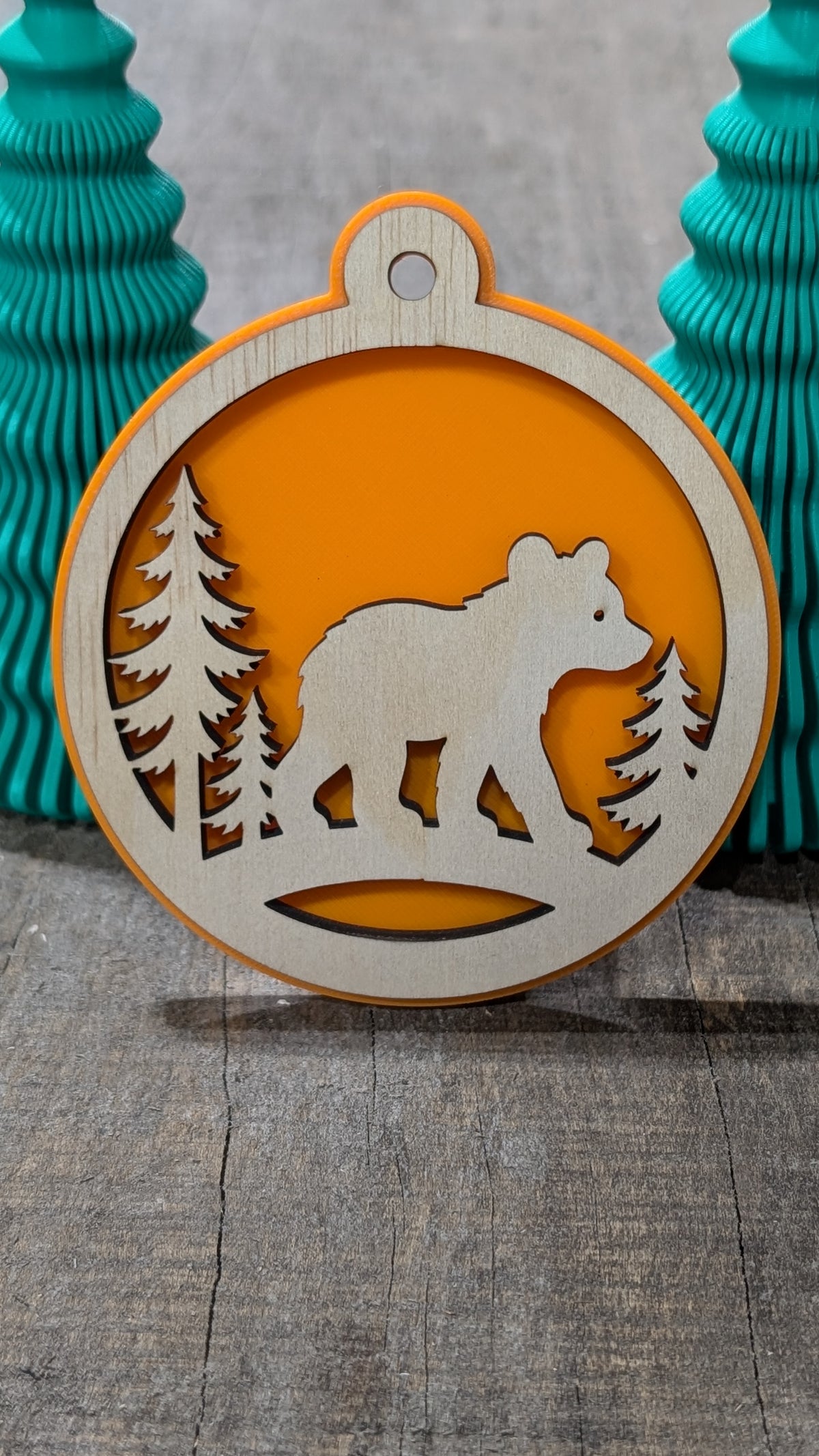 Boule de Noël avec ours et sapins en bois sur fond orange, fabriquée au Québec.