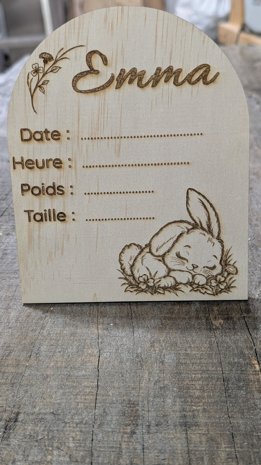 Plaque de naissance en bois en forme d’arche, prénom Emma, lapin endormi et fleurs, avec espaces pour les informations de naissance.